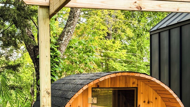 Een houten constructie met een ronde ingang, een bank ervoor en een donker gebouw op de achtergrond.