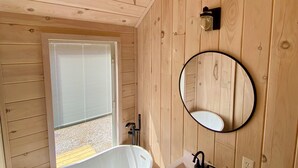 Een badkamer met houten lambrisering, een vrijstaand bad, een wastafel, een spiegel en een toilet.