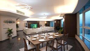 Uma sala de estar moderna com uma televisão de tela grande, uma área de jantar com mesa e cadeiras de madeira, e uma área de estar com sofás.