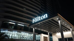Um hotel moderno com um grande letreiro 'Hilton', amplas janelas de vidro e um design arquitetônico contemporâneo.