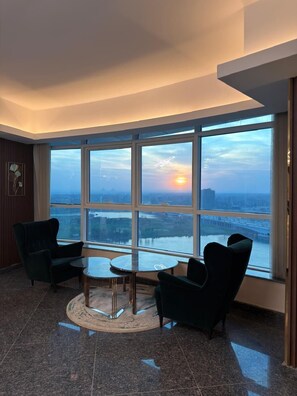 A modern hotel room with a large window offering a city view, a round glass table, two armchairs, and a decorative wall piece. - Hotel apartment in Hilton Nile Maadi with a charming Nile and pyramids view (Cairo Governorate)