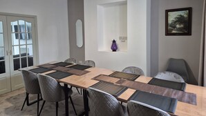 Un coin repas avec une longue table, des chaises rembourrées, un miroir et un tableau encadré accroché au mur.