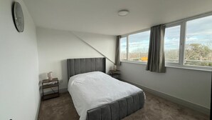 Une chambre à coucher avec un lit, une table de chevet, une lampe, une horloge et une fenêtre avec des rideaux.