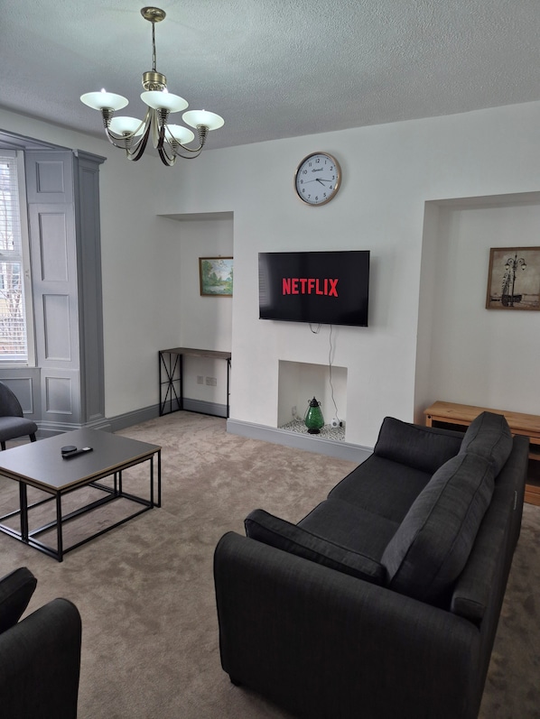 A living room with a sofa, coffee table, TV, and a clock on the wall. - Cosy Spacious Coastal Stay (South Shields)