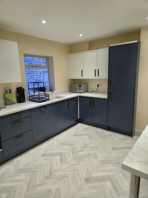A modern kitchen with a herringbone-patterned floor, white cabinets, and a built-in microwave. - Cosy Spacious Coastal Stay (South Shields)
