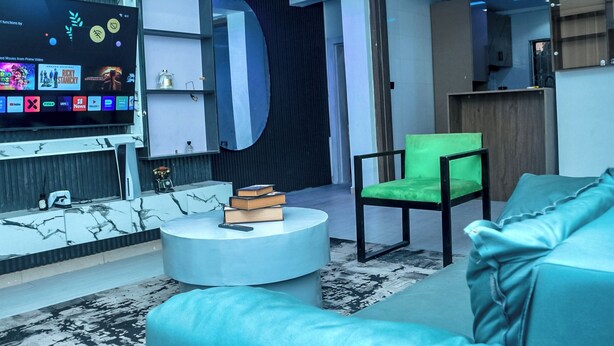 Una sala de estar moderna con un televisor de pantalla plana, una mesa de centro redonda, un sillón verde y un sofá.