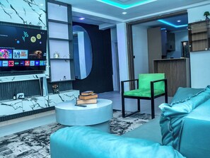 Un salon moderne avec un téléviseur à écran plat, une table basse ronde, un fauteuil vert et un canapé.