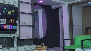 Una sala moderna con televisor de pantalla plana, una mesa redonda, un sillón verde y un espejo grande.