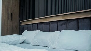 Una cama con ropa de cama blanca, un cabecero oscuro y un panel de madera encima.