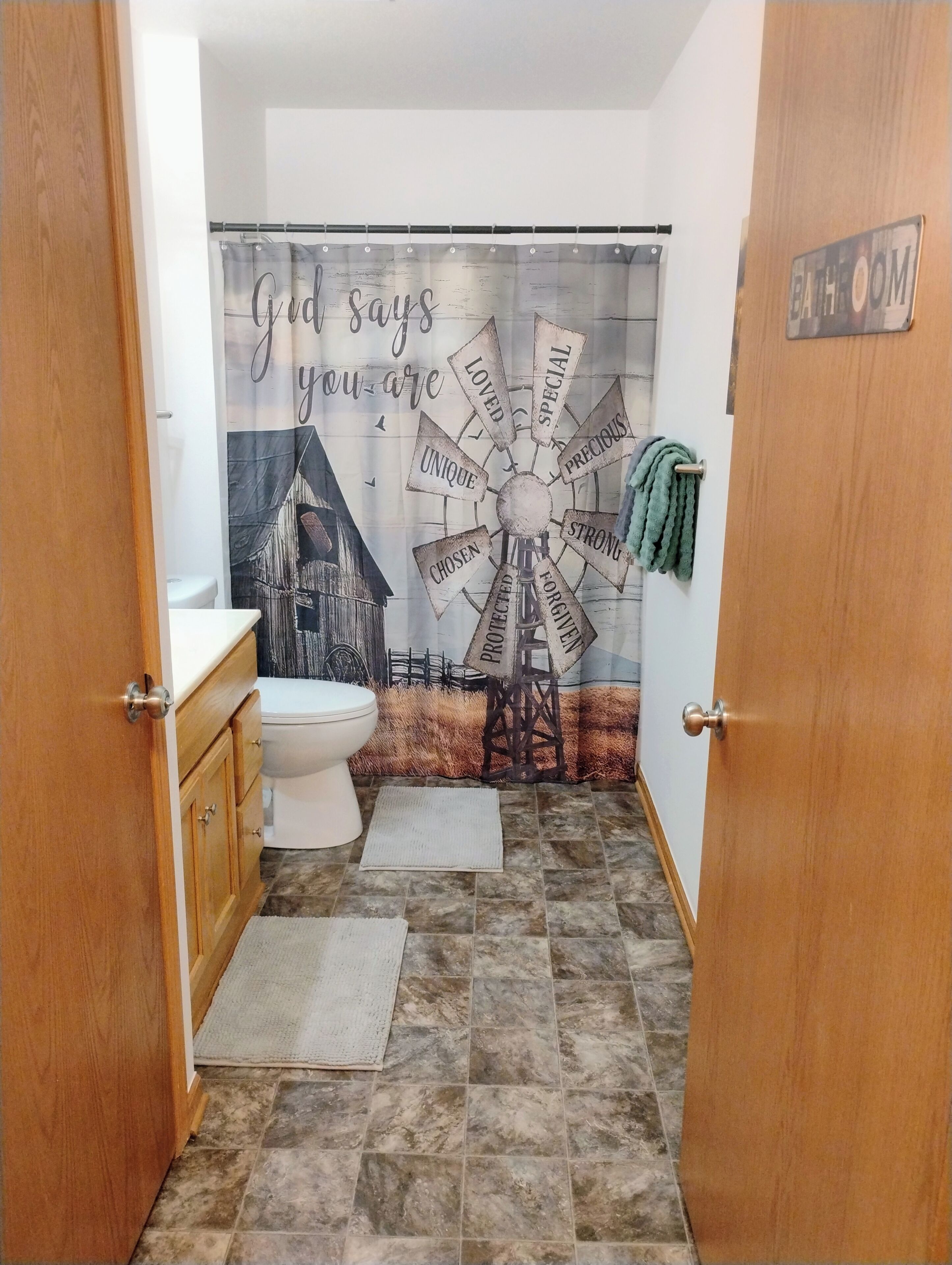 A bathroom with a windmill mural, a toilet, wooden cabinets, and a 'Bathroom' sign.