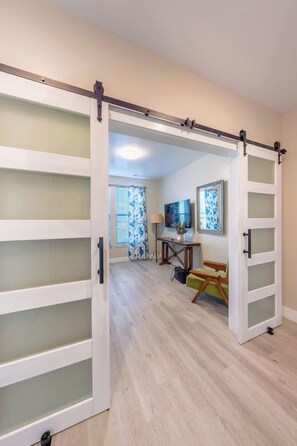Una habitación con puerta corredera que da a un comedor, una mesa con sillas y una ventana con persianas.