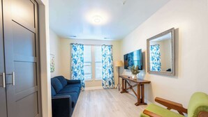 Una habitación con sofá, televisor, espejo y banca.