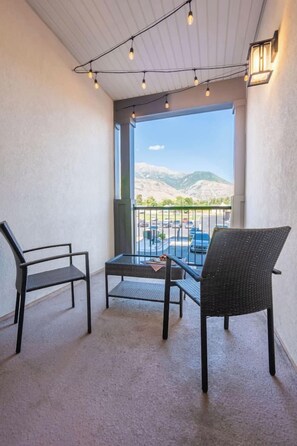 Un balcone con due sedie, un tavolino e vista su un parcheggio e montagne.