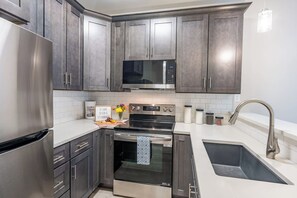 Una cocina moderna con electrodomésticos de acero inoxidable, armarios oscuros y encimera blanca.