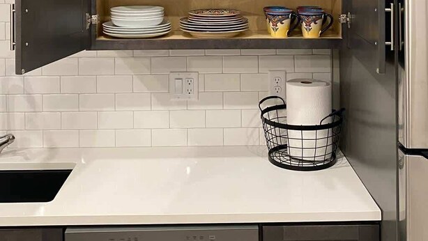Una cocina con un armario que contiene cuencos, platos, vasos y una cesta con servilletas de papel.