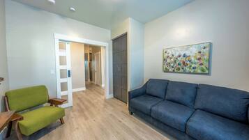 A living room with a green chair, a blue sofa, and a wooden bench. There is a door leading to another room and a painting on the wall.