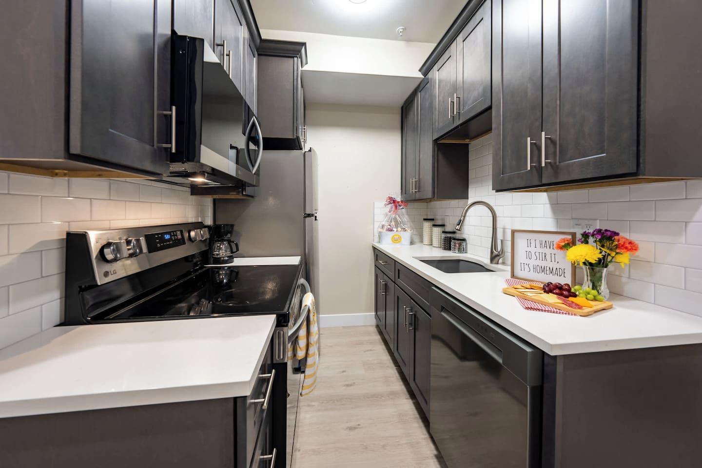 Una cocina moderna con muebles oscuros, estufa de acero inoxidable y encimera blanca.