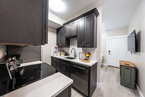 A modern kitchen with dark cabinets, a white countertop, and a built-in stove. - Cozy Main St Stay | King Bed + Loft Bed | Sleeps 3 (Pleasant Grove)