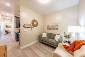 A living room with a sofa, a coffee table, a lamp, and a painting on the wall. - Cozy Main St Stay | King Bed + Loft Bed | Sleeps 3 (Pleasant Grove)
