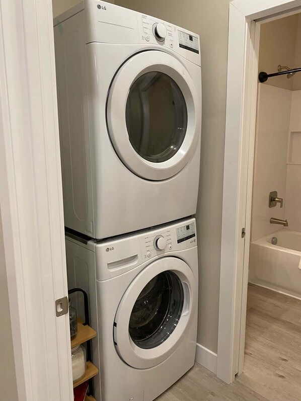 Lavatrice e asciugatrice impilate in un bagno, con una vasca da bagno sullo sfondo.