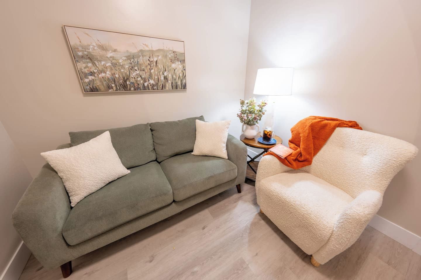 A living room with a sofa, a chair, a lamp, and a painting on the wall.