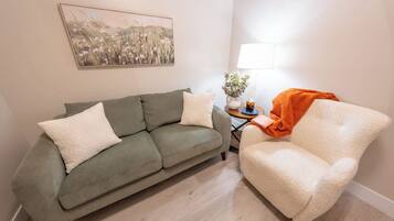 A living room with a sofa, a chair, a lamp, and a painting on the wall.