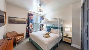 Ein Hotelzimmer mit Etagenbett, Schreibtisch, Stuhl, Nachttisch mit Lampe und einem Gemälde an der Wand.