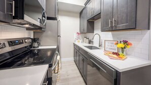 A modern kitchen with stainless steel appliances, dark cabinetry, and a white countertop. - Main St Suite | King Bed + Loft Bed | Full Kitchen (Pleasant Grove)