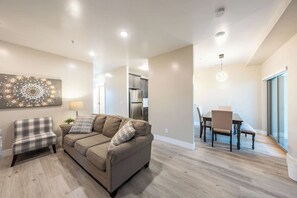 Ein modernes Wohnzimmer mit einer Couch, einem Esstisch mit Stühlen und einer Küchenzeile im Hintergrund.