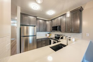 A modern kitchen with stainless steel appliances, dark wood cabinets, white countertops, and pendant lighting. - Historic Main St | 3BR Suite | Sleeps 6 (Pleasant Grove)