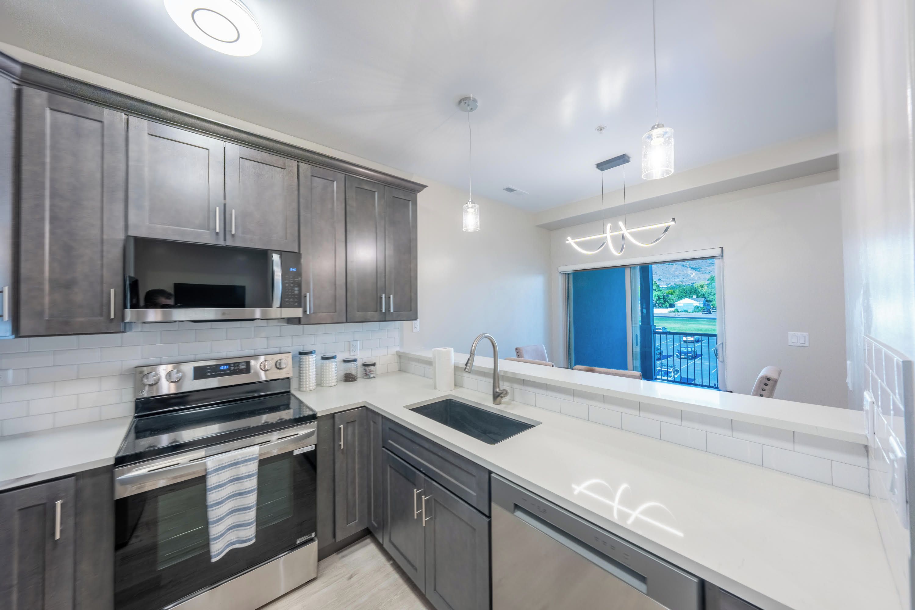A modern kitchen with stainless steel appliances, grey cabinets, and a large window offering a view of the outdoors.