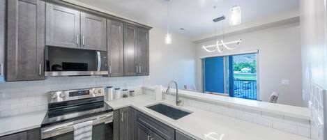 A modern kitchen with stainless steel appliances, grey cabinets, and a large window offering a view of the outdoors.