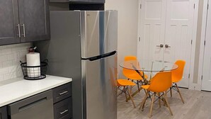 Een keuken met een roestvrijstalen koelkast, een wit aanrecht en een eettafel met vier oranje stoelen.
