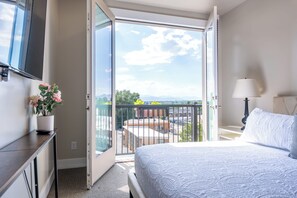 Ein Hotelzimmer mit Bett, Fernseher, Balkon mit Blick und einer Zimmerpflanze.