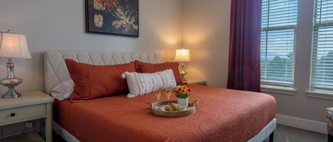 A hotel room with a large bed, two bedside lamps, a painting on the wall, and a window with curtains.