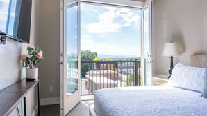 A hotel room with a bed, a TV, a balcony with a view, and a nightstand with a lamp.