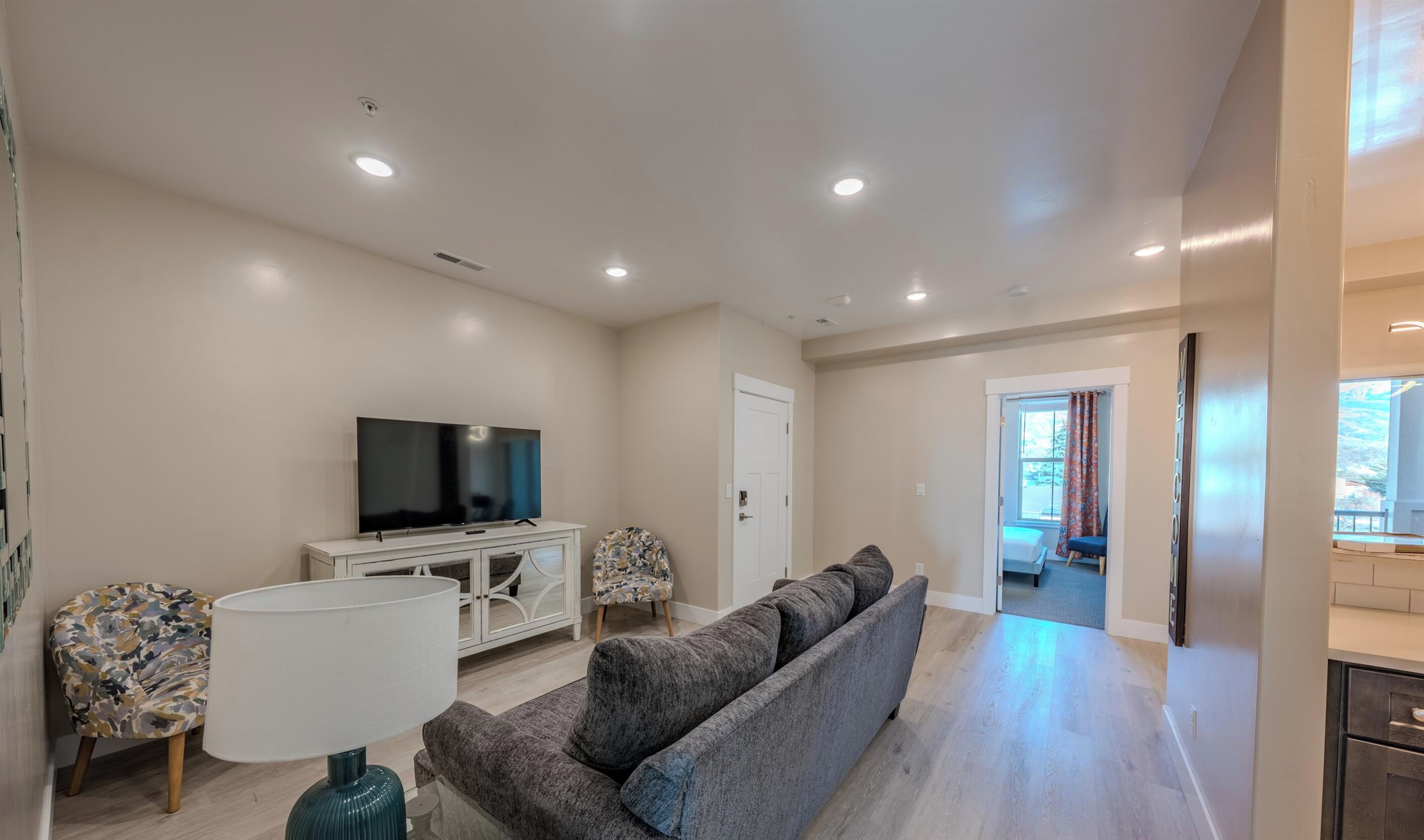 A modern living room with a flat-screen TV, a sofa, a lamp, and a patterned chair.