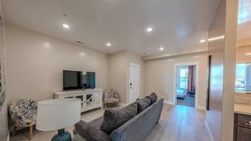 A modern living room with a flat-screen TV, a sofa, a lamp, and a patterned chair.