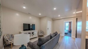 Una sala de estar con un sofá, un televisor, una lámpara y un mueble.