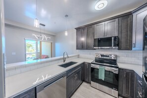 A modern kitchen with dark cabinets, stainless steel appliances, and a white countertop.