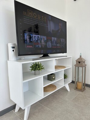 Een flatscreen televisie bevestigd aan een witte tv-meubel met planken, een kleine speaker en een decoratieve lantaarn.
