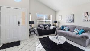 A living room with a black sofa, a grey sofa, a white coffee table, a black rug, a white door, and a window with blinds. - Spacious 4-bedroom Pool house in charming Kissimmee Close to Disney  with Wi-fi (Kissimmee)