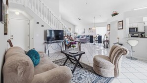 A spacious living area with a sofa, armchair, and a television. - Spacious 4-bedroom Pool house in charming Kissimmee Close to Disney  with Wi-fi (Kissimmee)