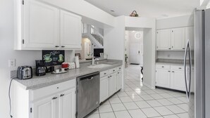 A modern kitchen with white cabinets, a dishwasher, a coffee maker, and a stainless steel refrigerator. - Spacious 4-bedroom Pool house in charming Kissimmee Close to Disney  with Wi-fi (Kissimmee)
