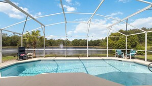 A covered swimming pool with a view of a lake, lounge chairs, and a chair with a red cushion. - Spacious 4-bedroom Pool house in charming Kissimmee Close to Disney  with Wi-fi (Kissimmee)