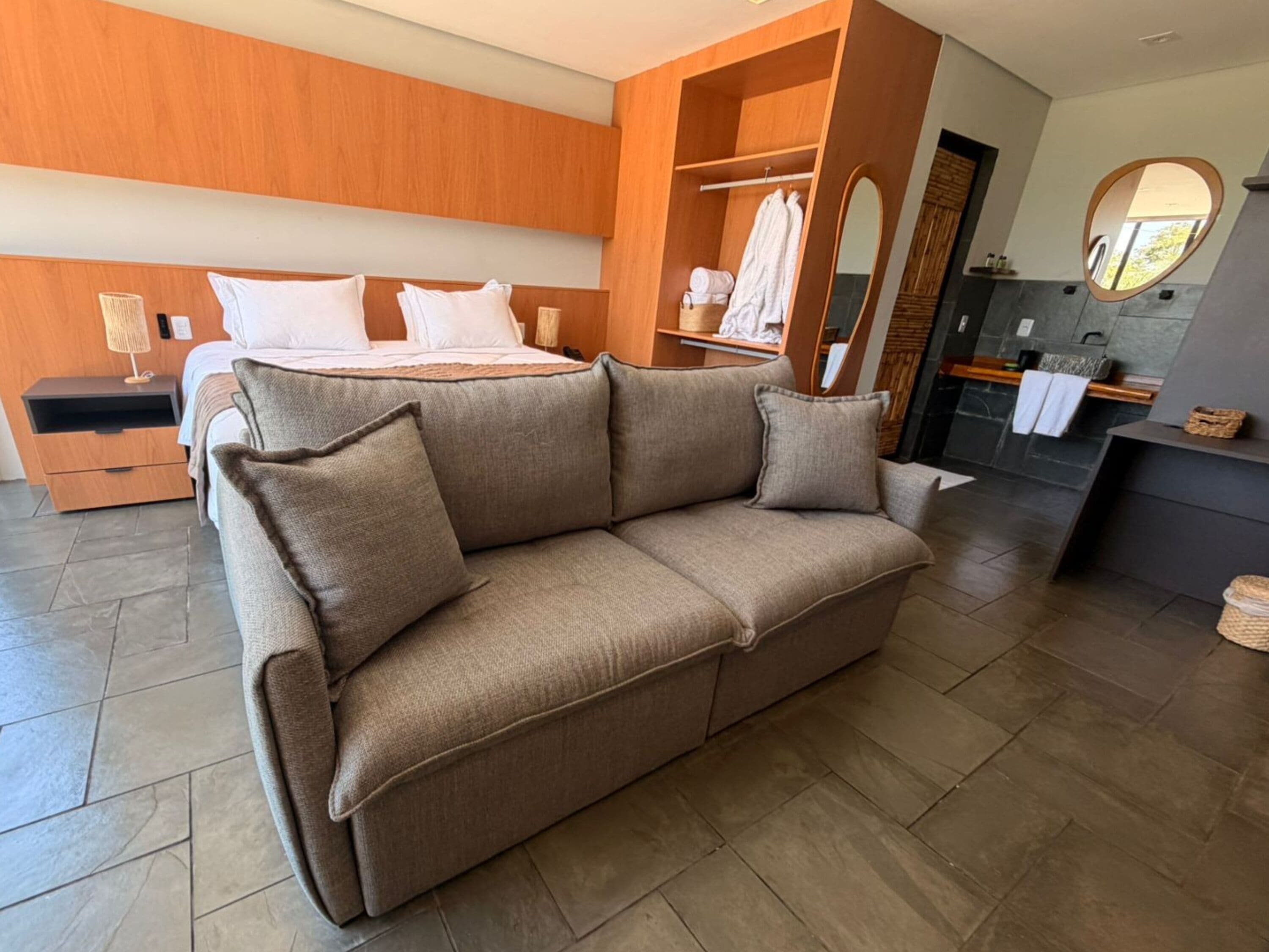 A modern hotel room with a sofa, a bed, a nightstand, a mirror, and a bathroom area.