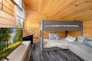 Un lit superposé avec une structure grise, un canapé gris et un téléviseur posé sur un meuble.
