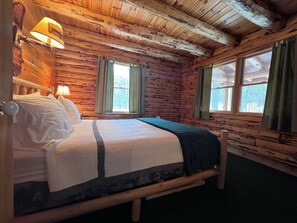 Ein Schlafzimmer in einer Holzhütte mit einem Bett, zwei Fenstern und Holzboden.