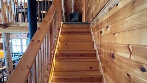 Eine hölzerne Treppe mit Geländer, ein Fernseher auf der Landung und ein Blick ins Freie durch die Fenster.