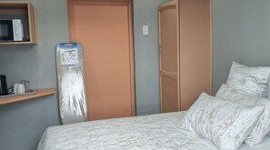 Un dormitorio con una cama, un armario de madera, un microondas en un estante y una puerta.